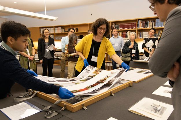 A group of people stand around a table displaying photos and archival material in the Getty Research Institute's special collections seminar room.